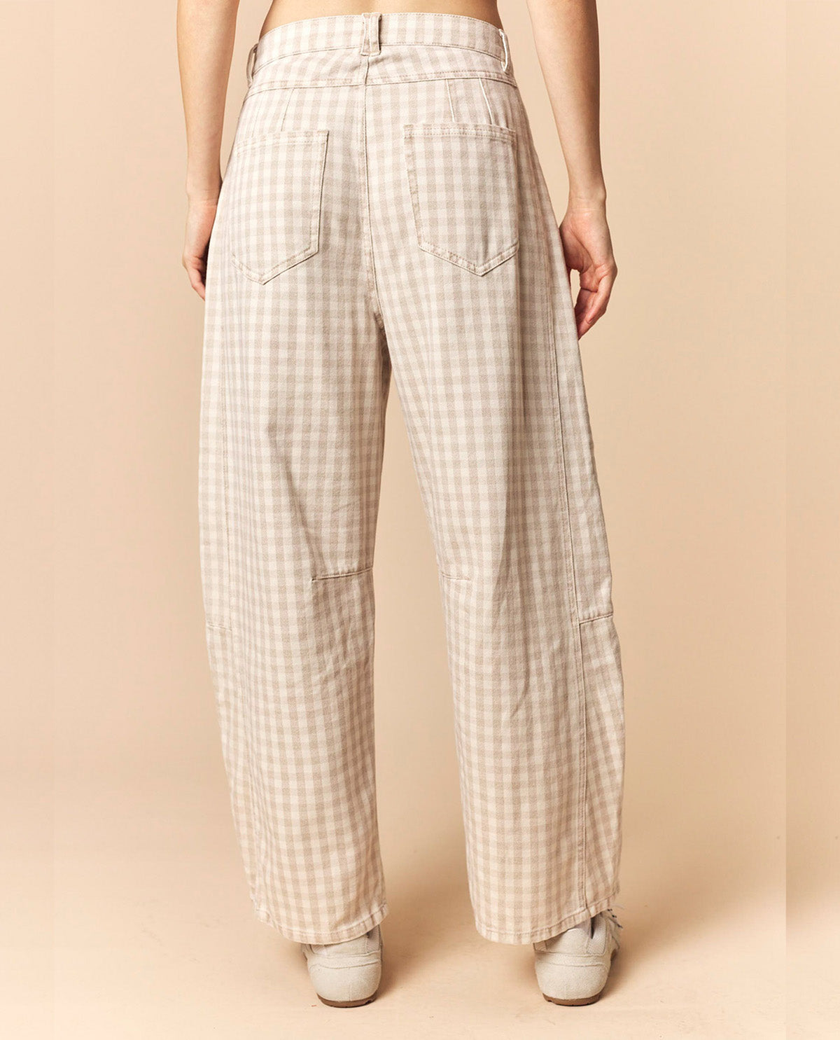 A person shown from the back wearing wide-leg trousers with a beige and white gingham check pattern, paired with white sneakers, against a solid beige studio background.