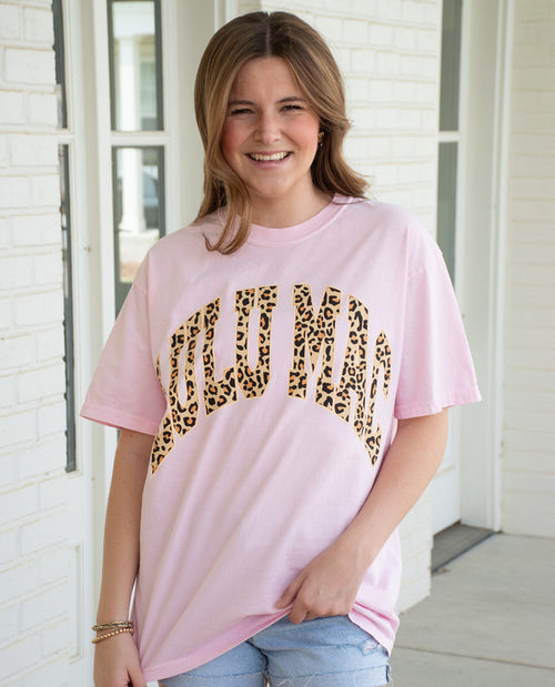 Person wearing a pink t-shirt with leopard print text outdoors.