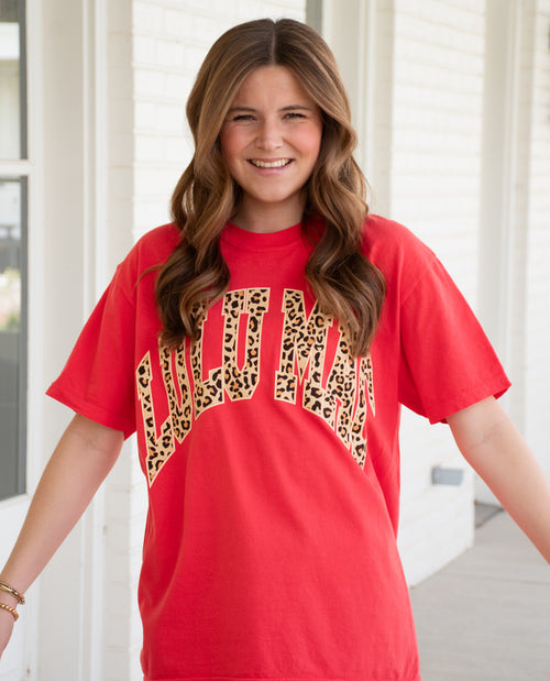Person wearing a red t-shirt with leopard print text in an indoor setting