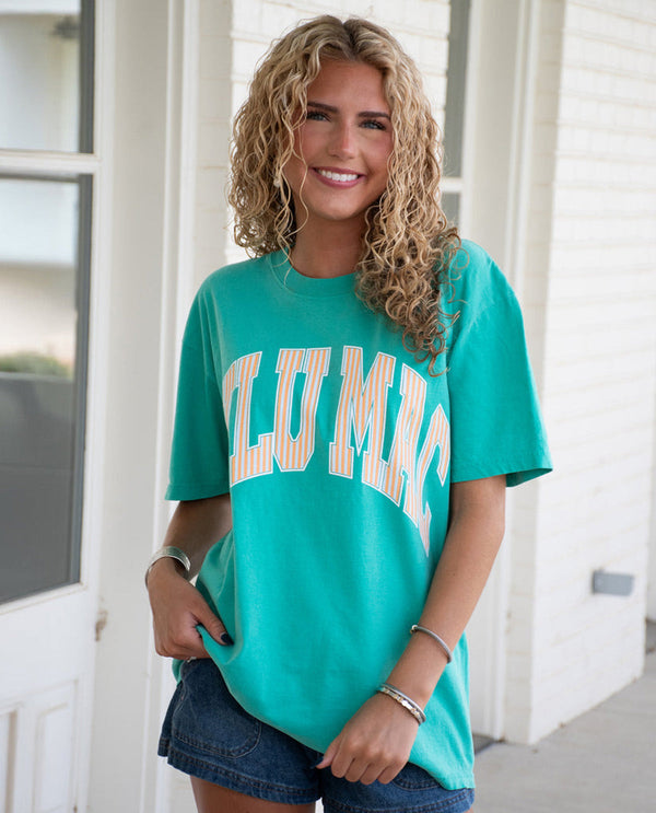 Woman wearing a teal t-shirt with 'LULU MAC' text, standing outdoors.