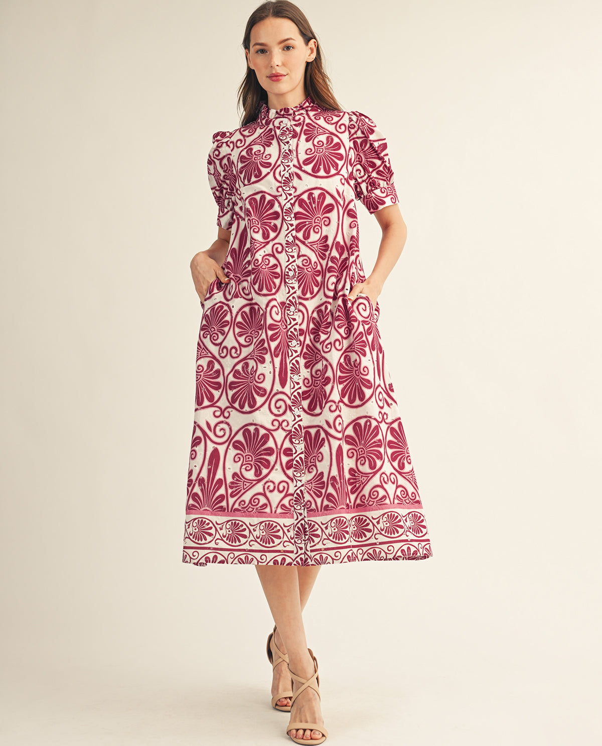 A woman modeling a short-sleeve midi dress with a pink and white floral block-print pattern, standing against a solid light beige background.
