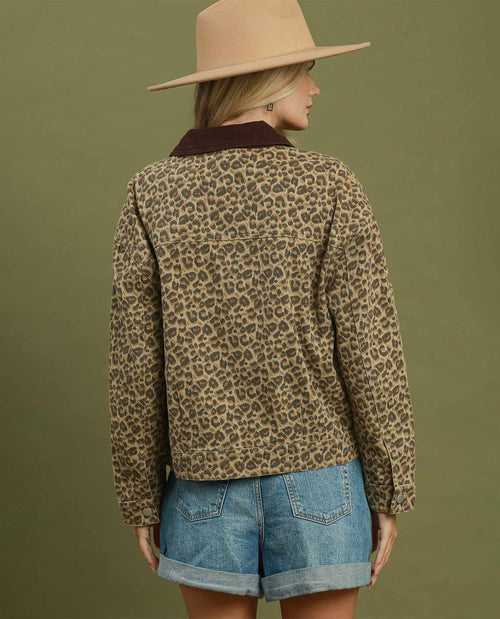 A woman shown from the back wearing a leopard-print long-sleeve shirt jacket with a dark brown corduroy collar, paired with denim shorts and a beige wide-brim hat, against a solid olive green background.