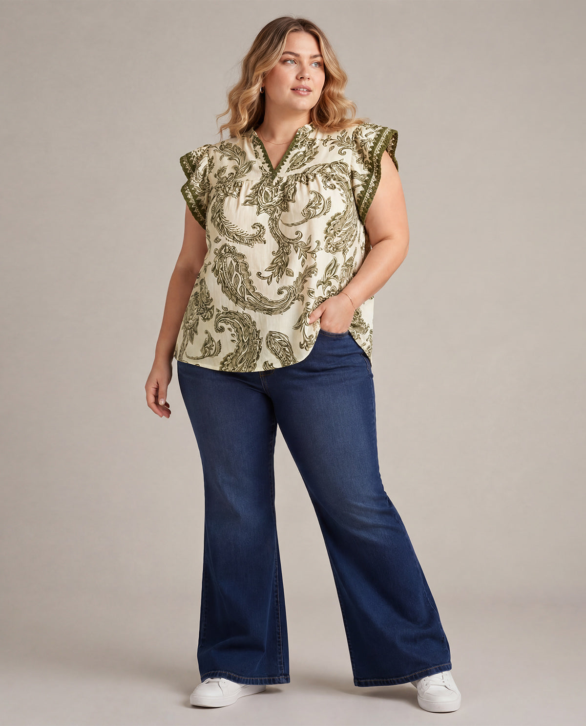 Woman wearing a patterned top and blue jeans on a plain background