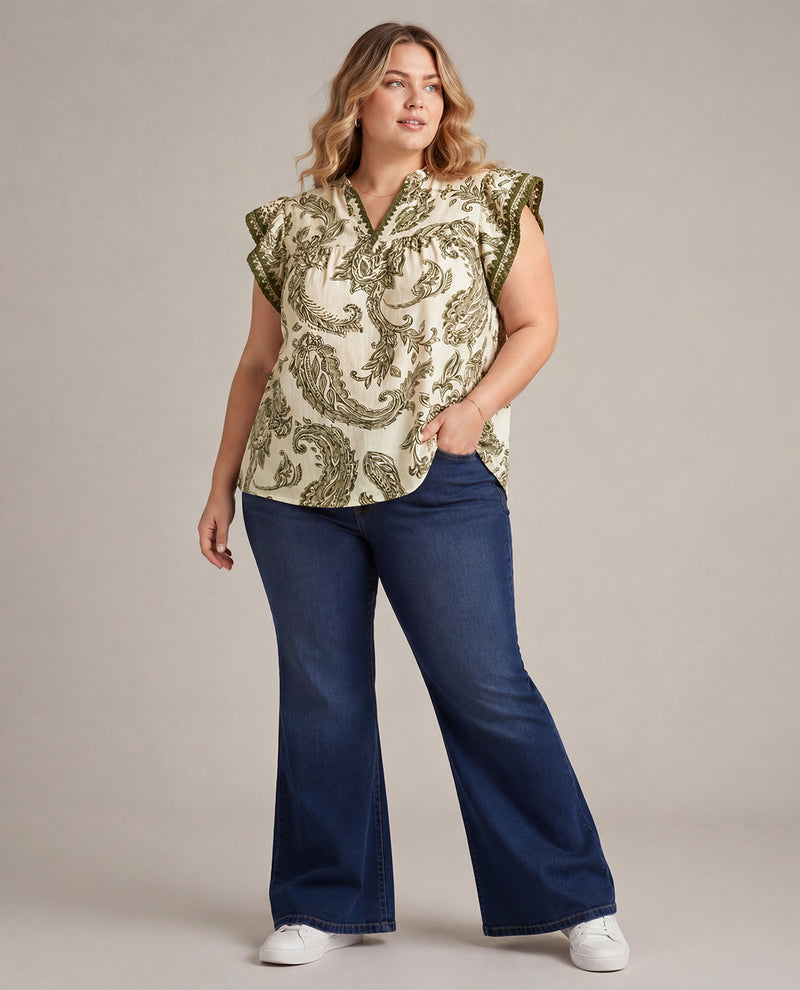 Woman wearing a patterned top and blue jeans on a plain background