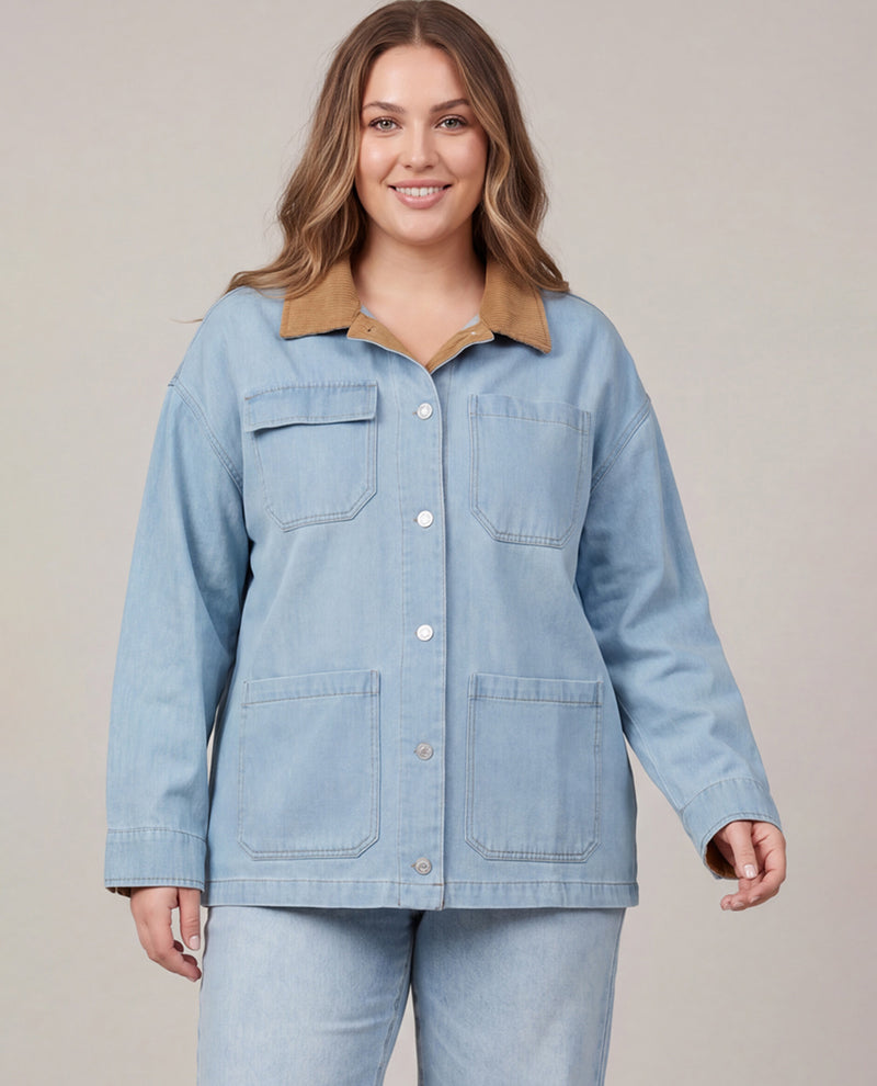 A woman modeling a light blue denim utility jacket with a tan collar, paired with matching light blue jeans, against a solid beige studio background.