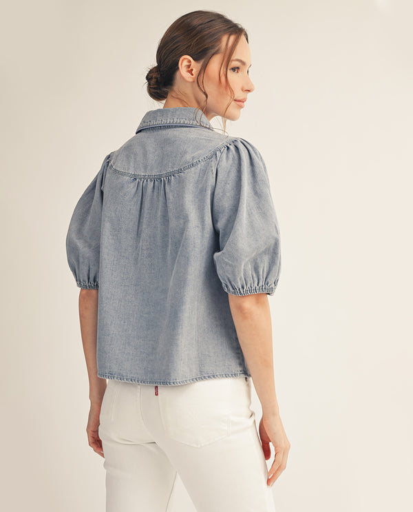 Woman wearing a light blue denim shirt with balloon sleeves on a beige background