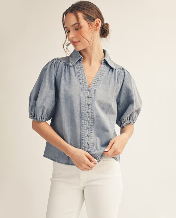 Woman wearing a light blue denim blouse with puff sleeves on a beige background