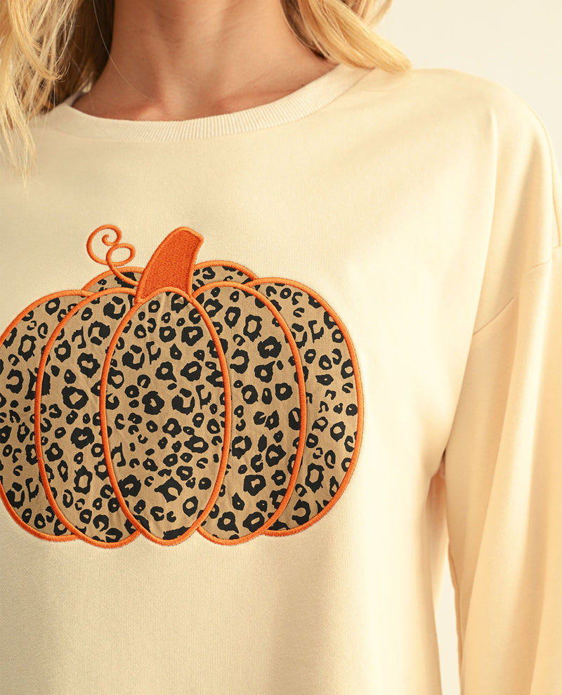 A close-up of a person wearing a cream-colored crewneck sweatshirt with a large leopard-print pumpkin applique on the front.