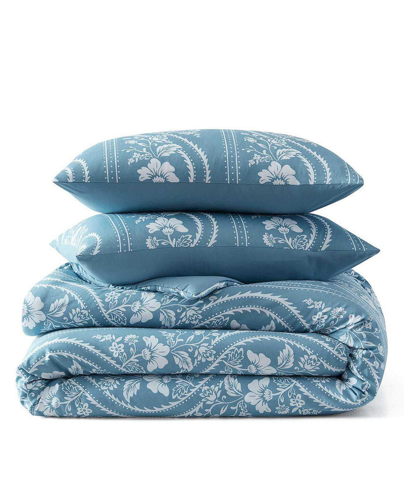 A folded bedding set consisting of a duvet cover and two matching pillowcases, all featuring a blue and white floral and scroll pattern, set against a plain white background.