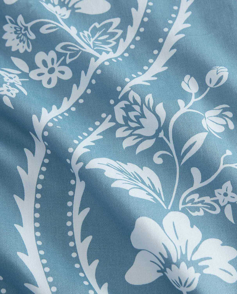 A close-up of a light blue fabric with a white floral and vine pattern, showing soft folds and texture.