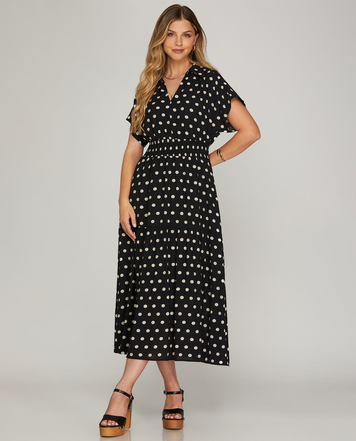 Woman wearing a black dress with white polka dots on a plain background