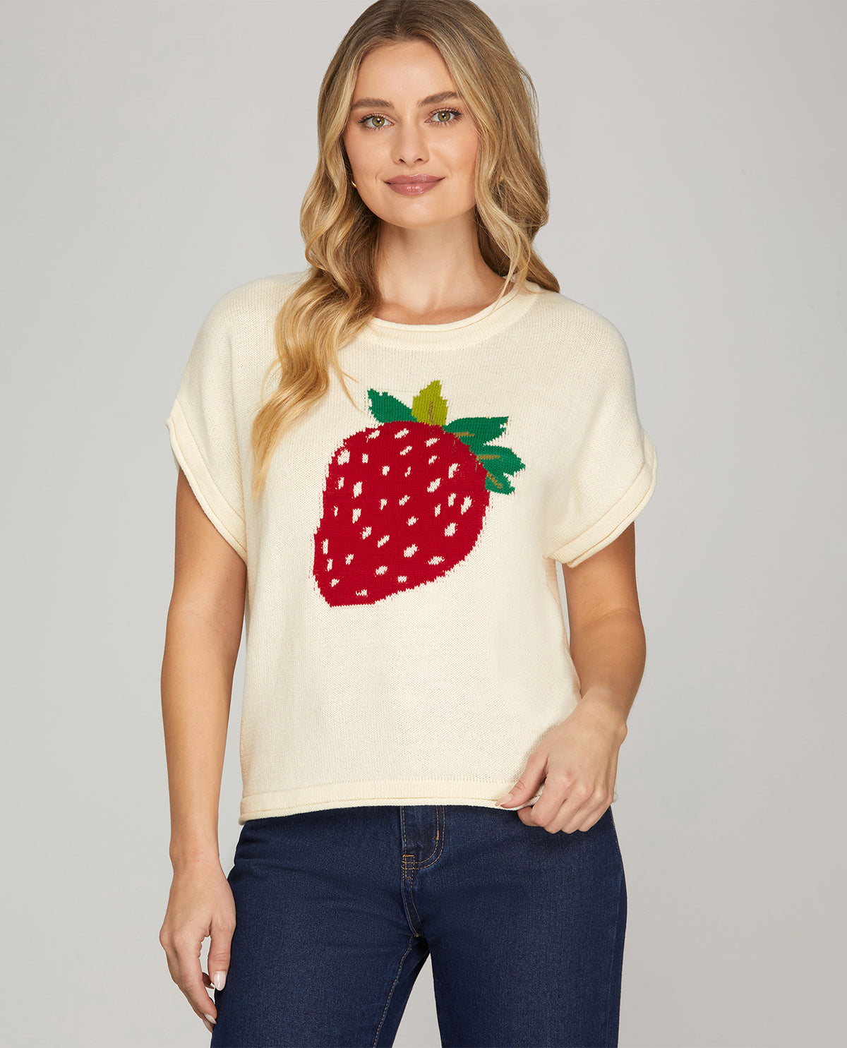Woman wearing a cream t-shirt with a strawberry design on a plain background