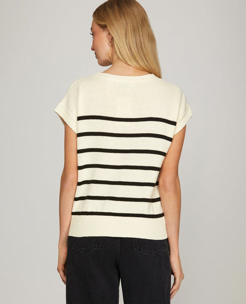 A woman shown from the back wearing a cream knit short-sleeve top with horizontal black stripes and dark jeans, against a plain light gray studio background.
