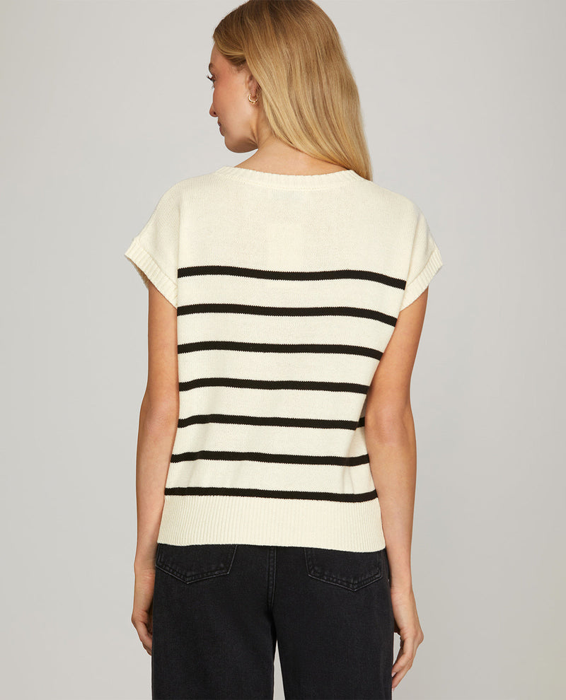 A woman shown from the back wearing a cream knit short-sleeve top with horizontal black stripes and dark jeans, against a plain light gray studio background.