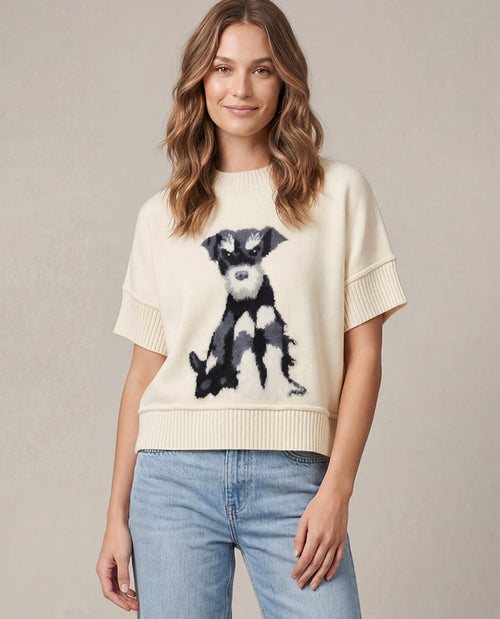 A woman wearing a cream-colored short-sleeve knit sweater with a black and white dog graphic on the front, paired with light blue jeans, against a neutral beige background.