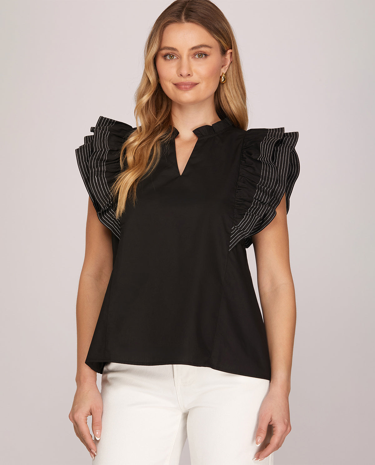 Woman wearing a black blouse with ruffled shoulders against a plain background