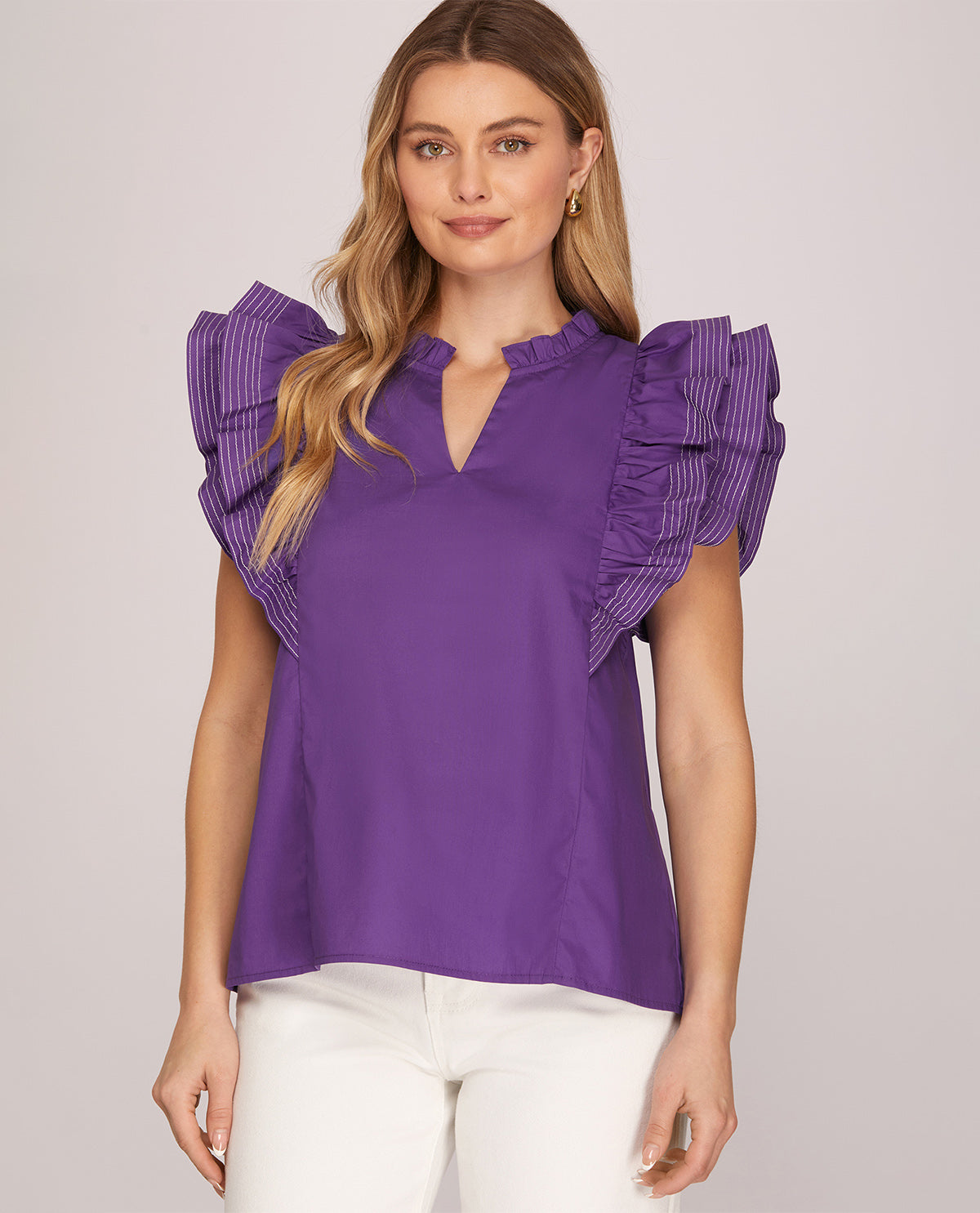 Woman wearing a purple blouse with ruffled sleeves on a plain background