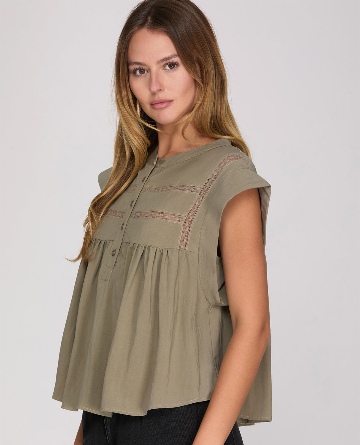 Woman wearing a green sleeveless top with embroidered details on a white background