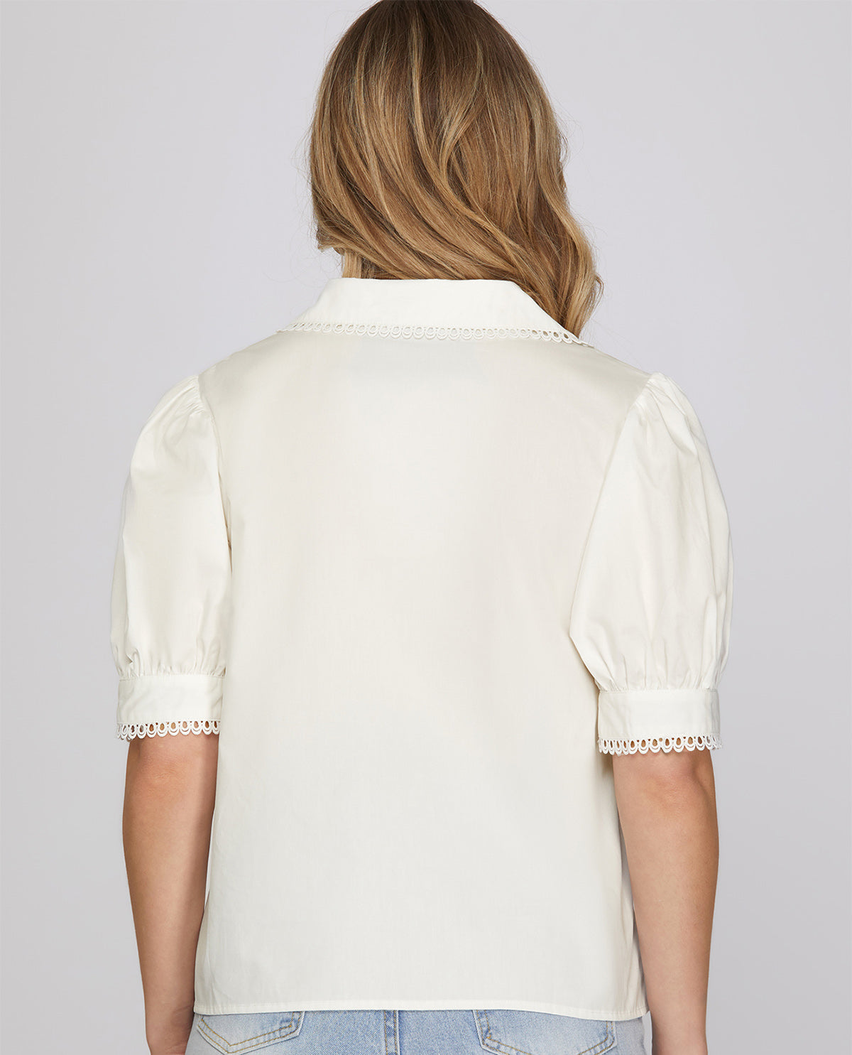 Person wearing a white blouse with lace trim on a plain background