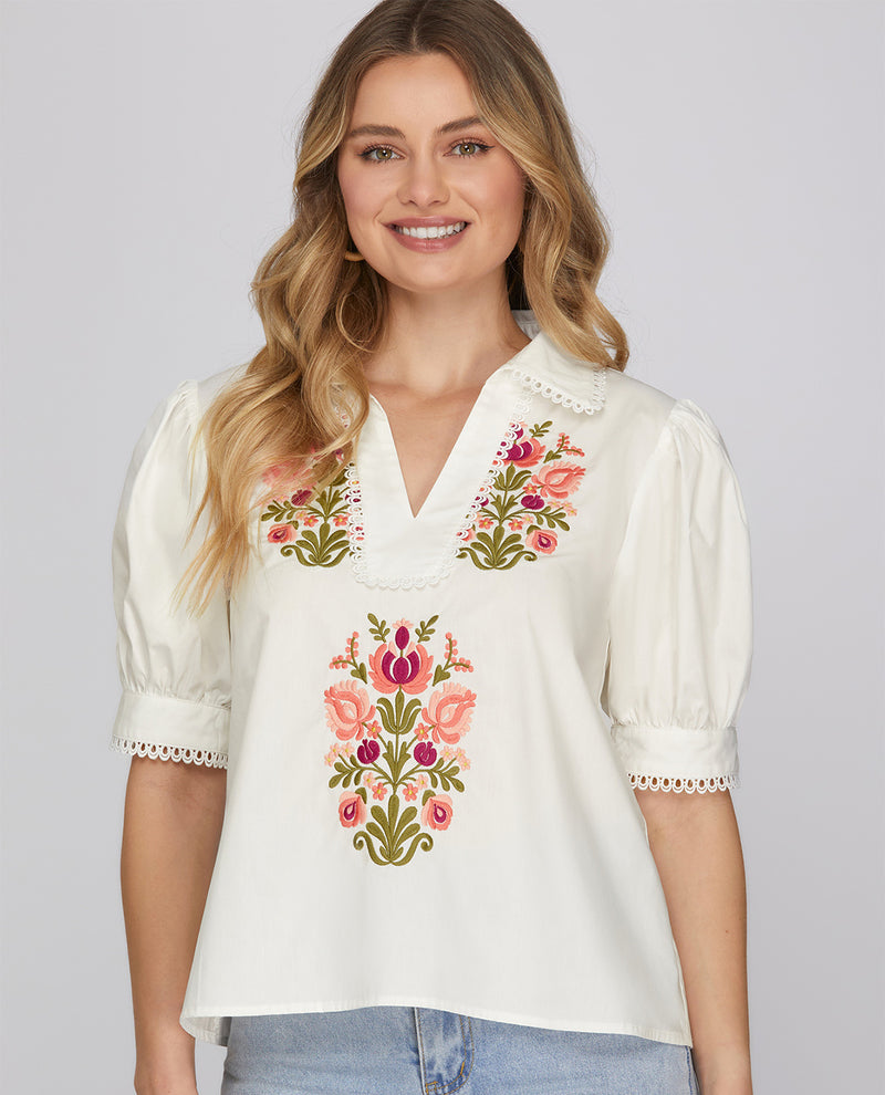 Woman wearing a white blouse with floral embroidery on a plain background