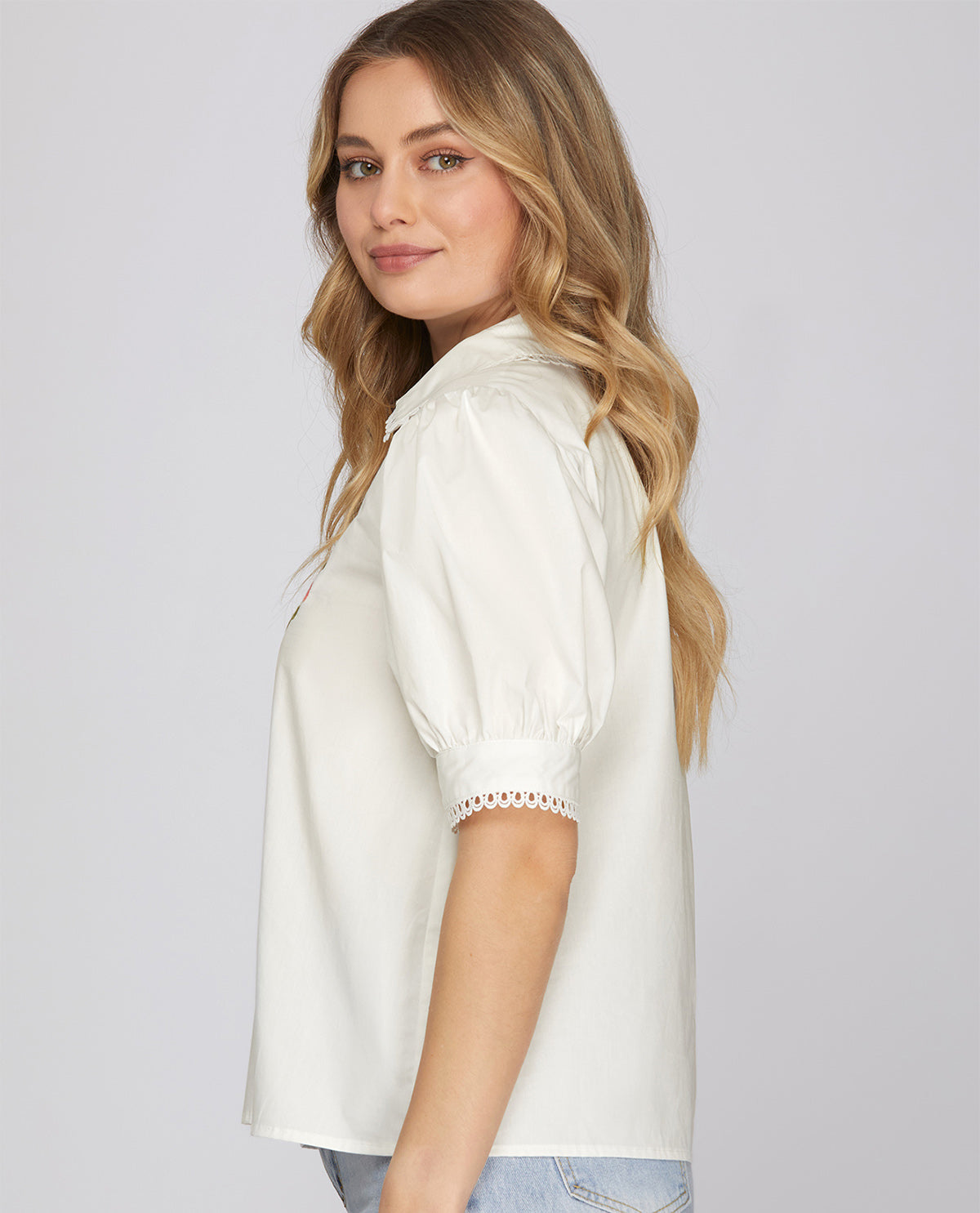 Woman wearing a white blouse with lace trim on a plain background