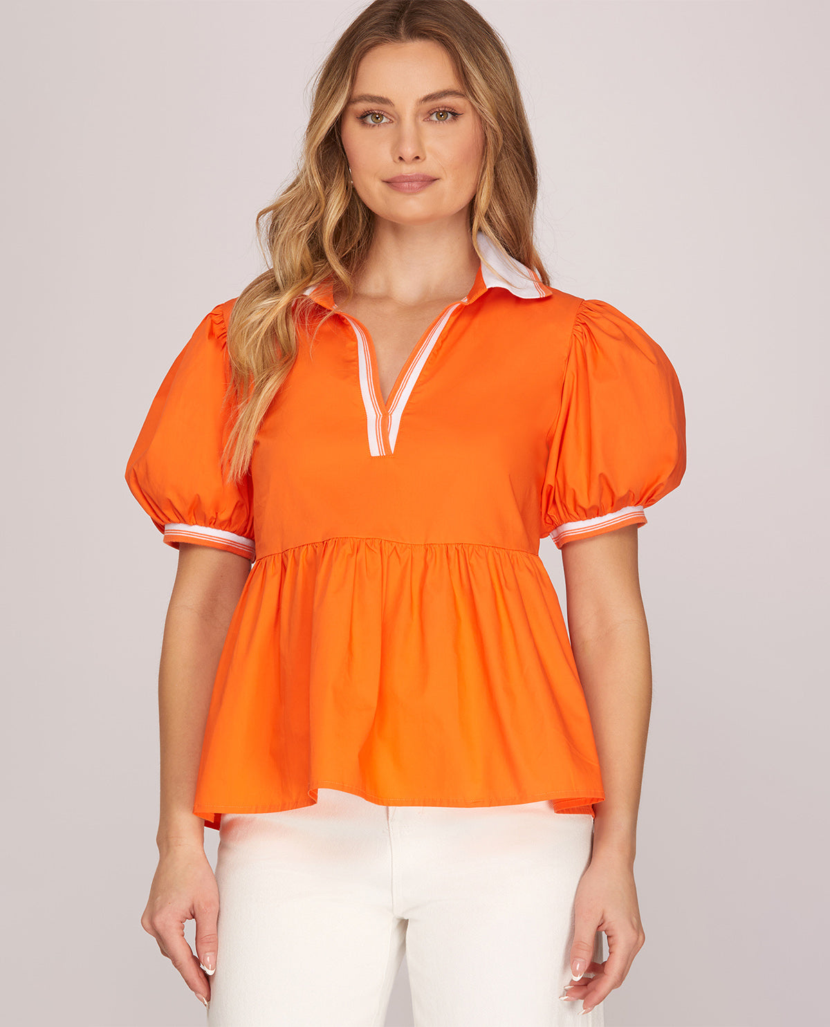 Woman wearing an orange blouse with puff sleeves against a plain background