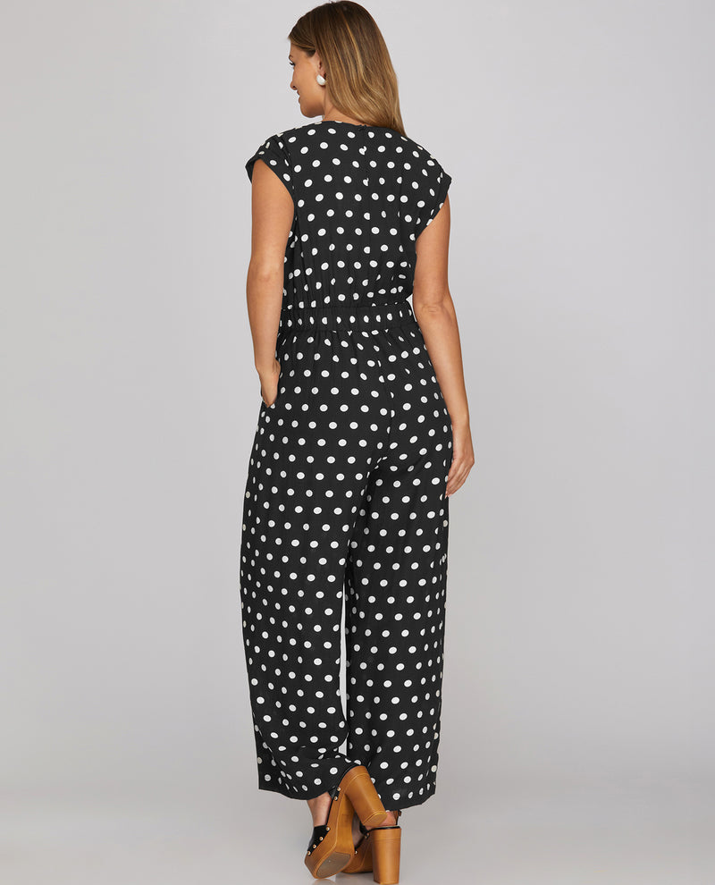 Woman wearing a black polka dot jumpsuit on a plain background