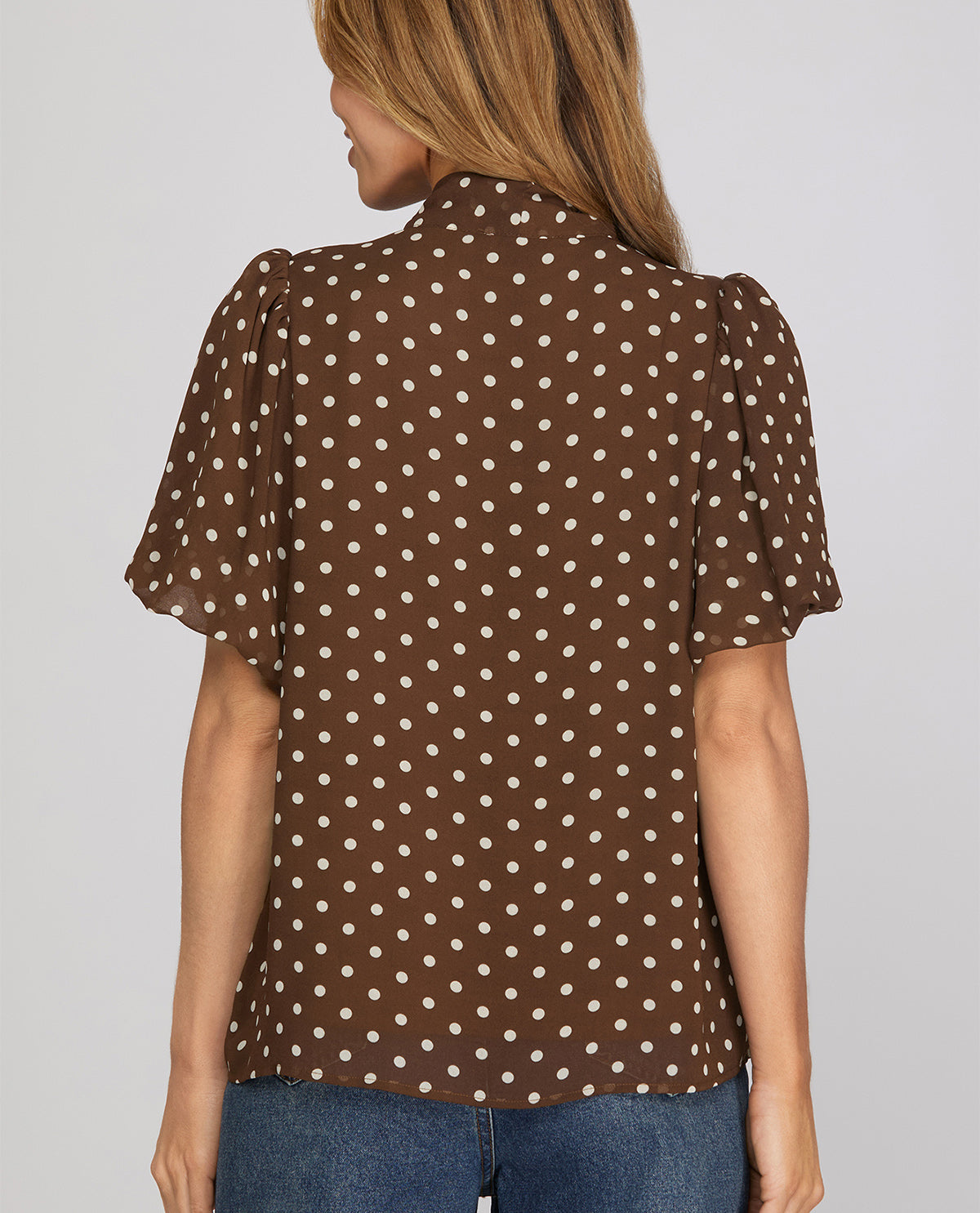 Woman wearing a brown polka dot blouse against a gray background