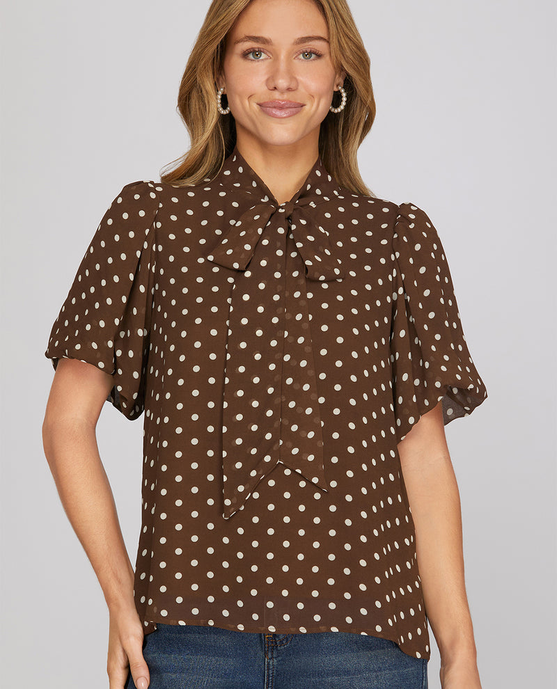 Woman wearing a brown polka dot blouse against a gray background