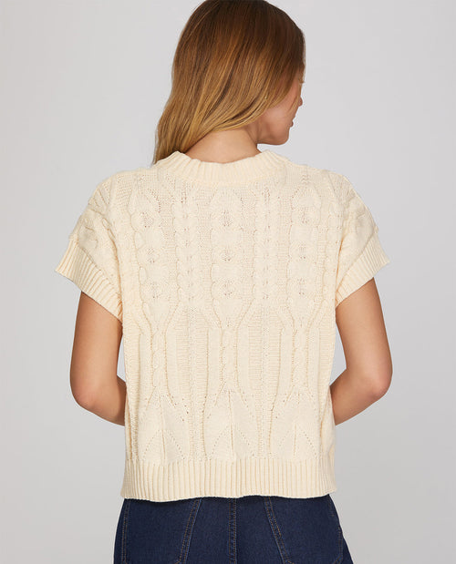 Woman wearing a cream-colored cable knit sweater against a plain background