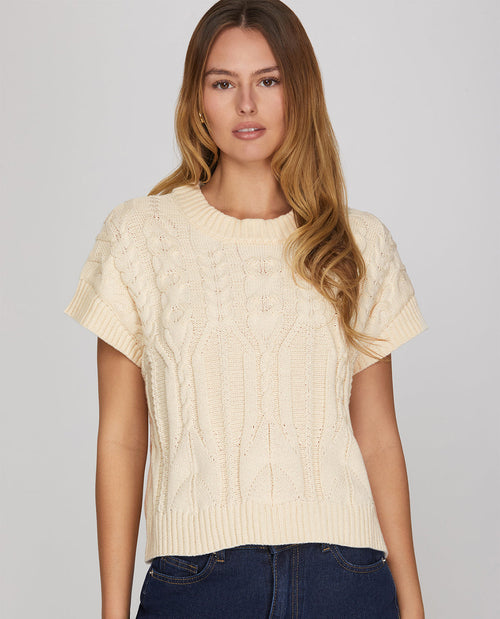 Woman wearing a beige cable knit short-sleeve sweater against a plain background