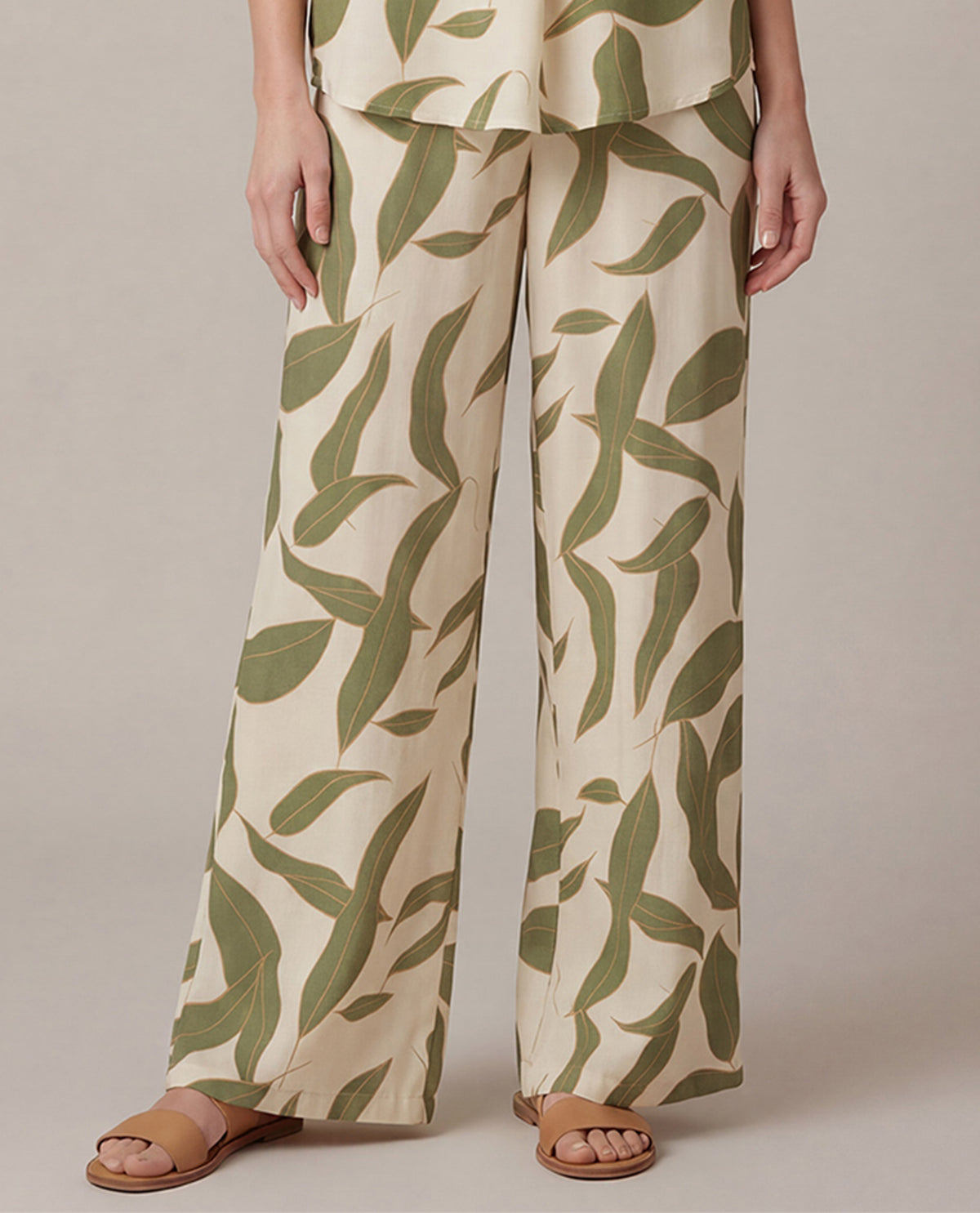 Person wearing a pair of wide-leg pants with a green leaf pattern on a neutral background