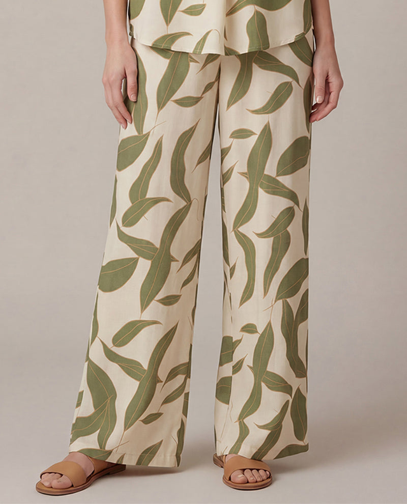 Person wearing a pair of wide-leg pants with a green leaf pattern on a neutral background