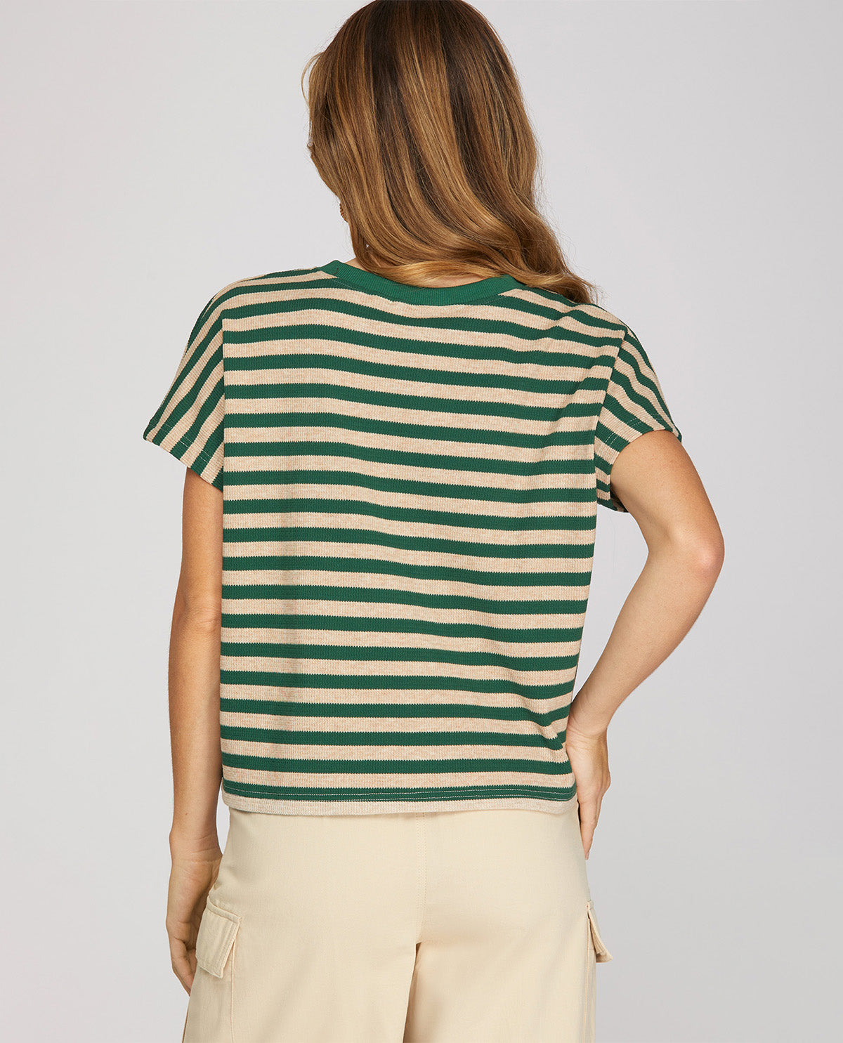 A woman shown from the back wearing a green and beige horizontally striped short-sleeve crop top and light beige cargo pants, against a solid light gray background.