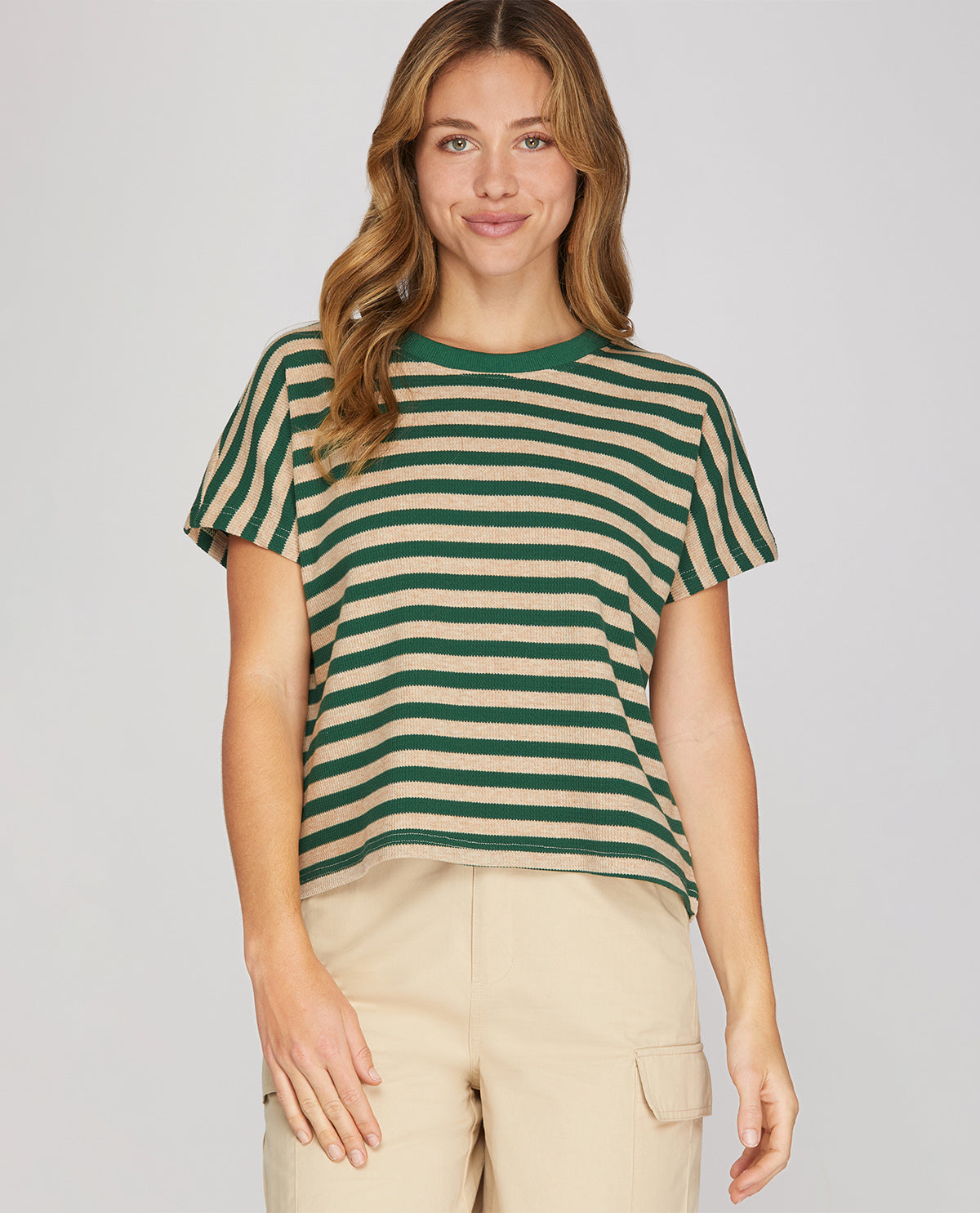 A woman wearing a green and beige horizontally striped short-sleeve crop top with beige cargo pants, standing against a light gray studio background.