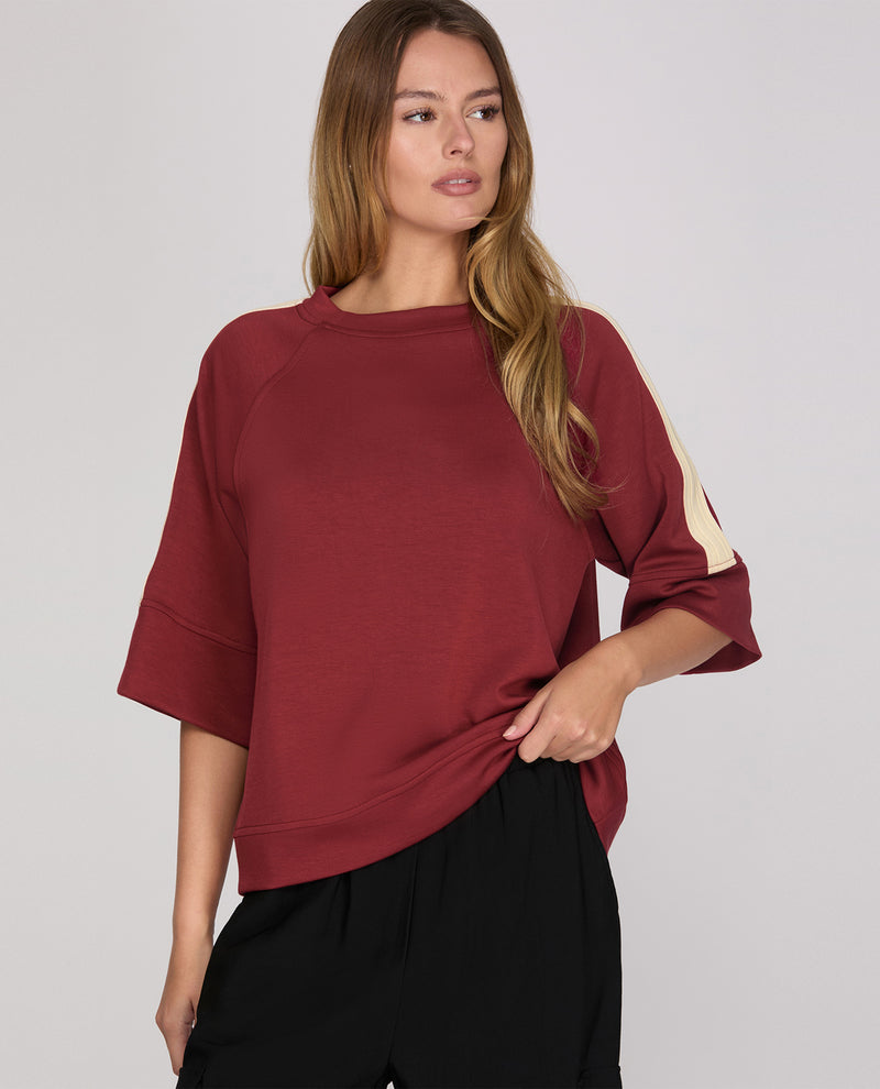 Woman wearing a burgundy oversized sweater with a plain background
