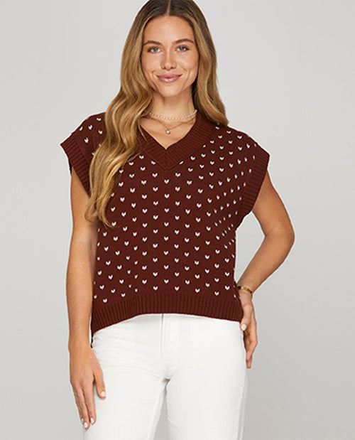 Woman wearing a brown sleeveless patterned top against a plain background