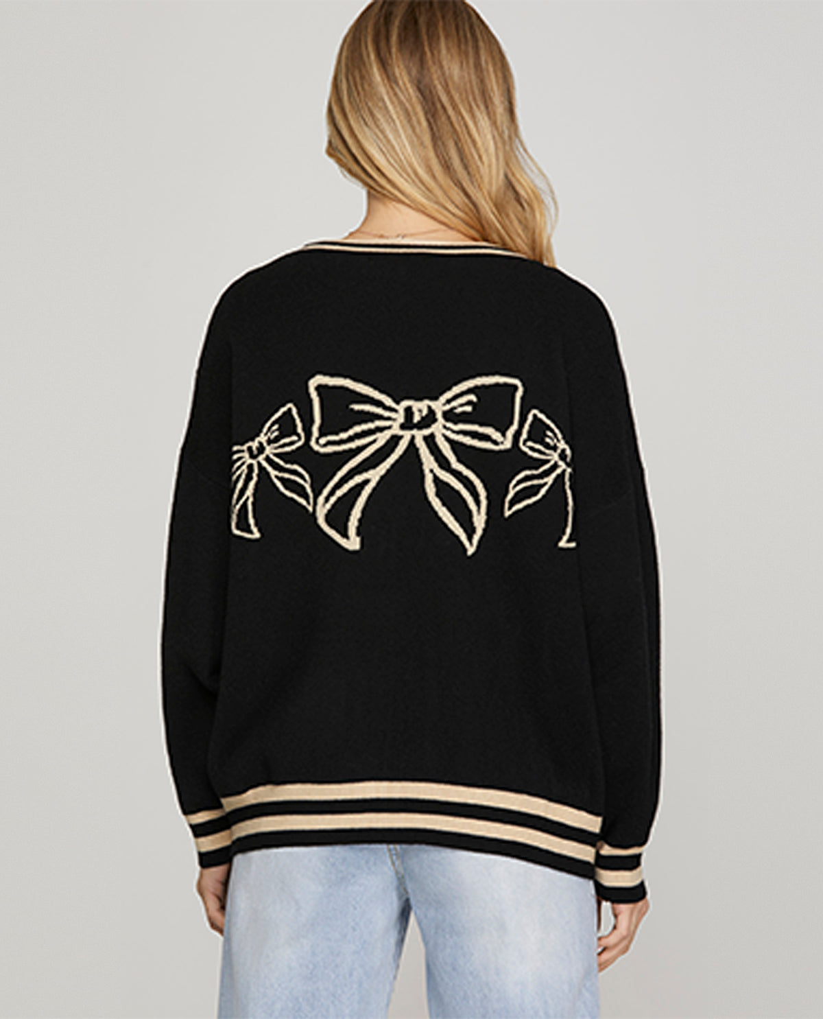 Black sweater with bow designs on the back worn by a person against a gray background