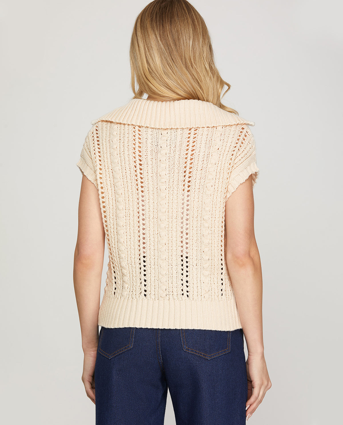 Woman wearing a beige knitted vest on a plain background