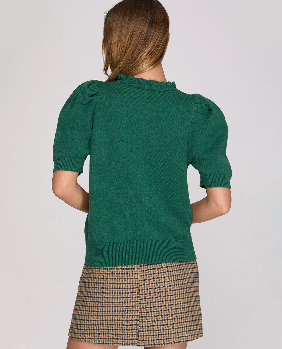 Person wearing a green sweater with puff sleeves and a plaid skirt on a plain background