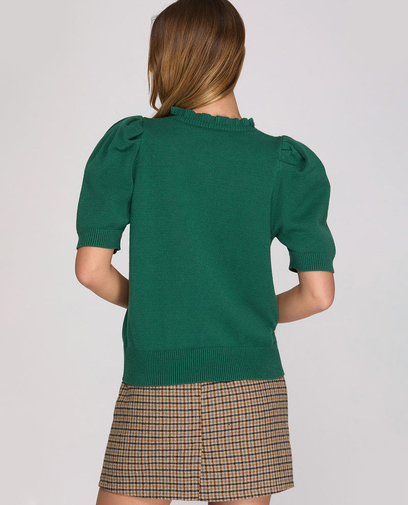 Person wearing a green sweater with puff sleeves and a plaid skirt on a plain background