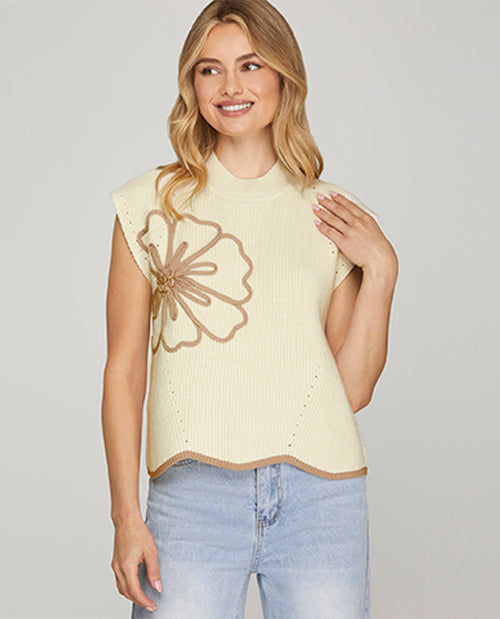Woman wearing a light-colored sleeveless top with a floral design on a plain background