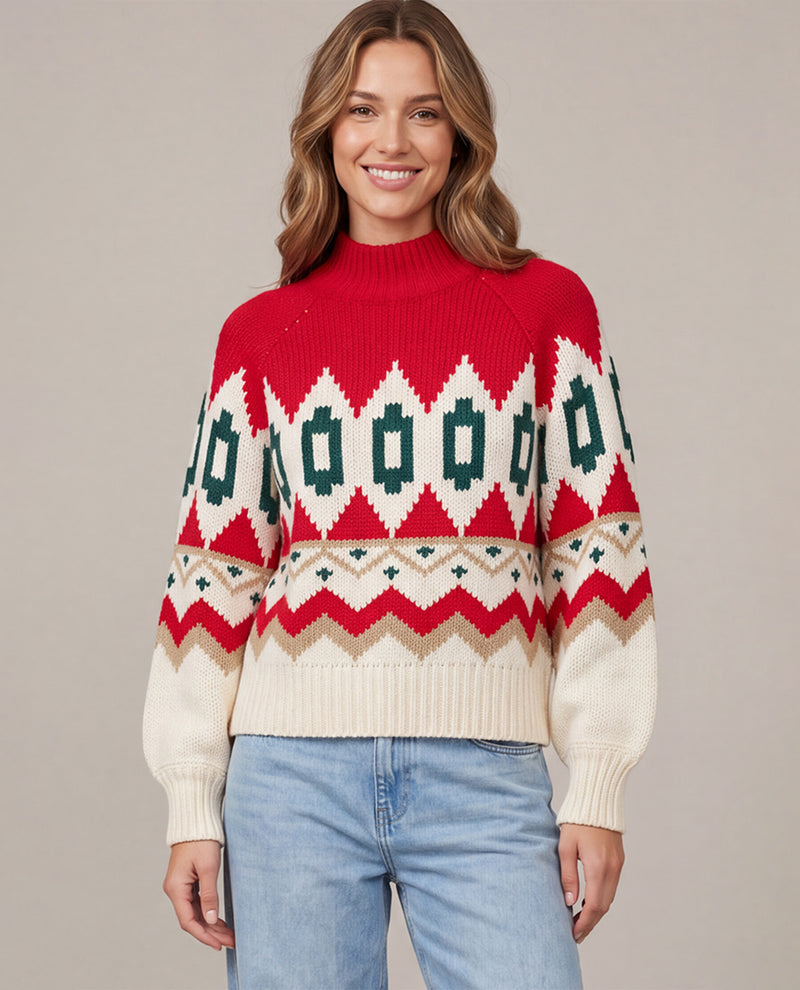 A woman wearing a red, cream, and green Fair Isle knit sweater with light blue jeans, standing against a solid beige studio background.