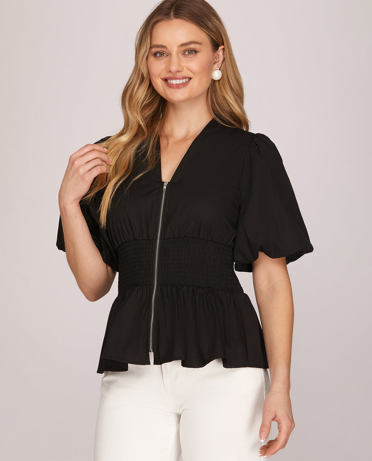 Woman wearing a black peplum top with white pants on a plain background