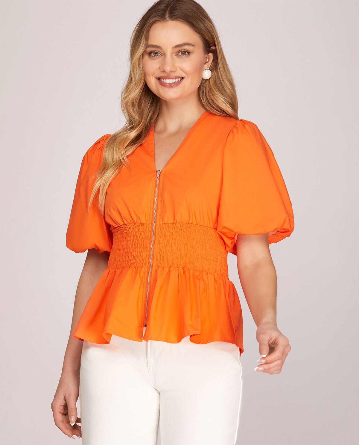 Woman wearing an orange puff-sleeve top against a light background