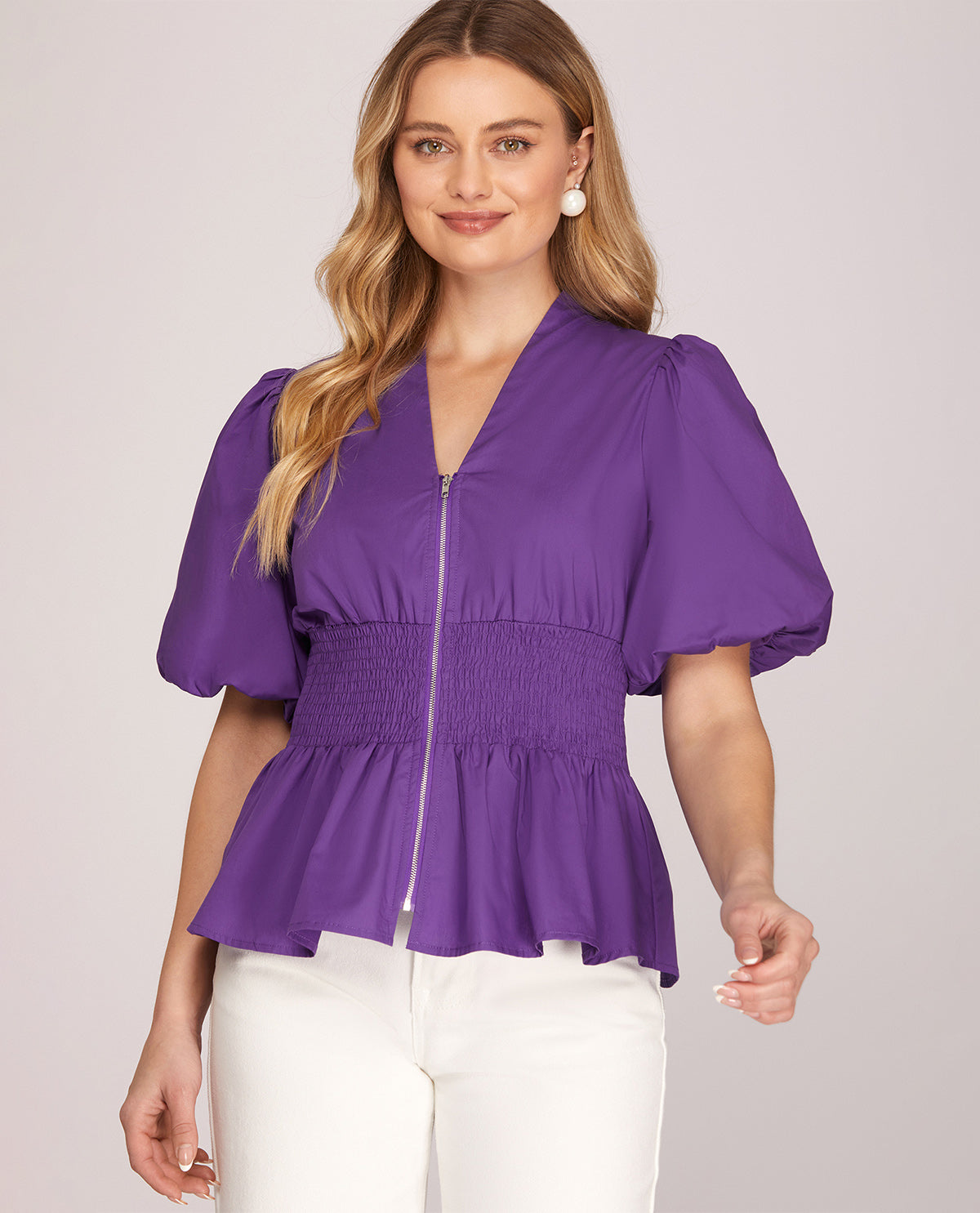 Woman wearing a purple zip-up top with puff sleeves on a light gray background