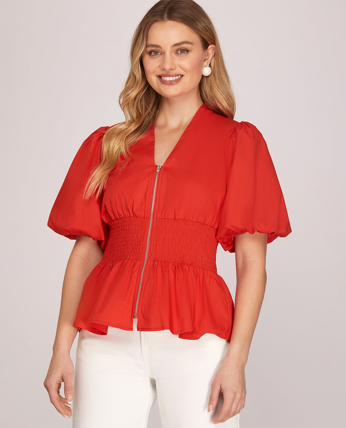 Woman wearing a red blouse with puff sleeves on a plain background