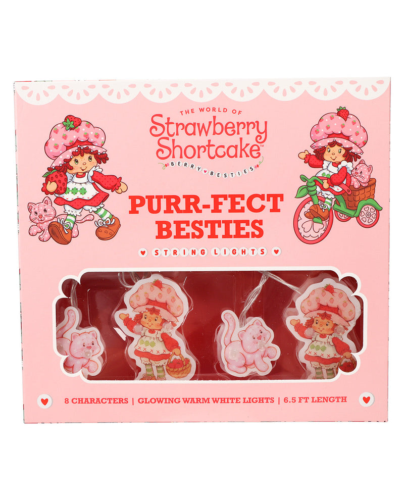 Strawberry Shortcake 'Purr-Fect Besties' string lights in a pink retail box. The package contains four glow-in-the-dark character-shaped string lights shaped like Strawberry Shortcake, a pink pig, and a pink bunny, visible through a clear window on a pink background.