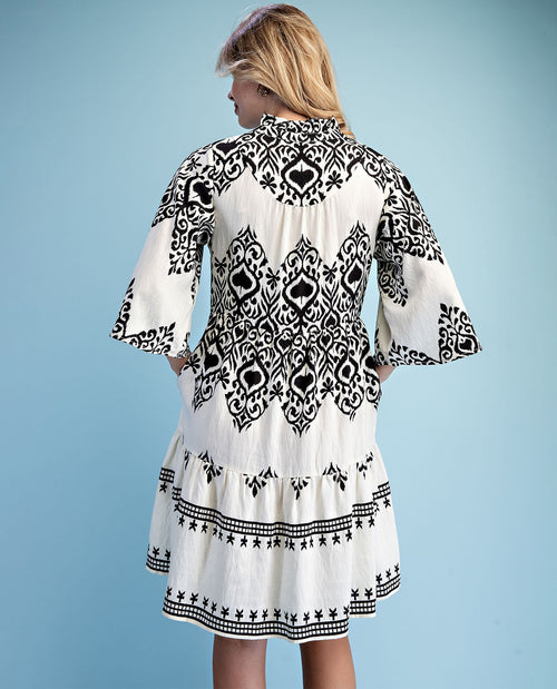 Woman wearing a white dress with black pattern on a light blue background