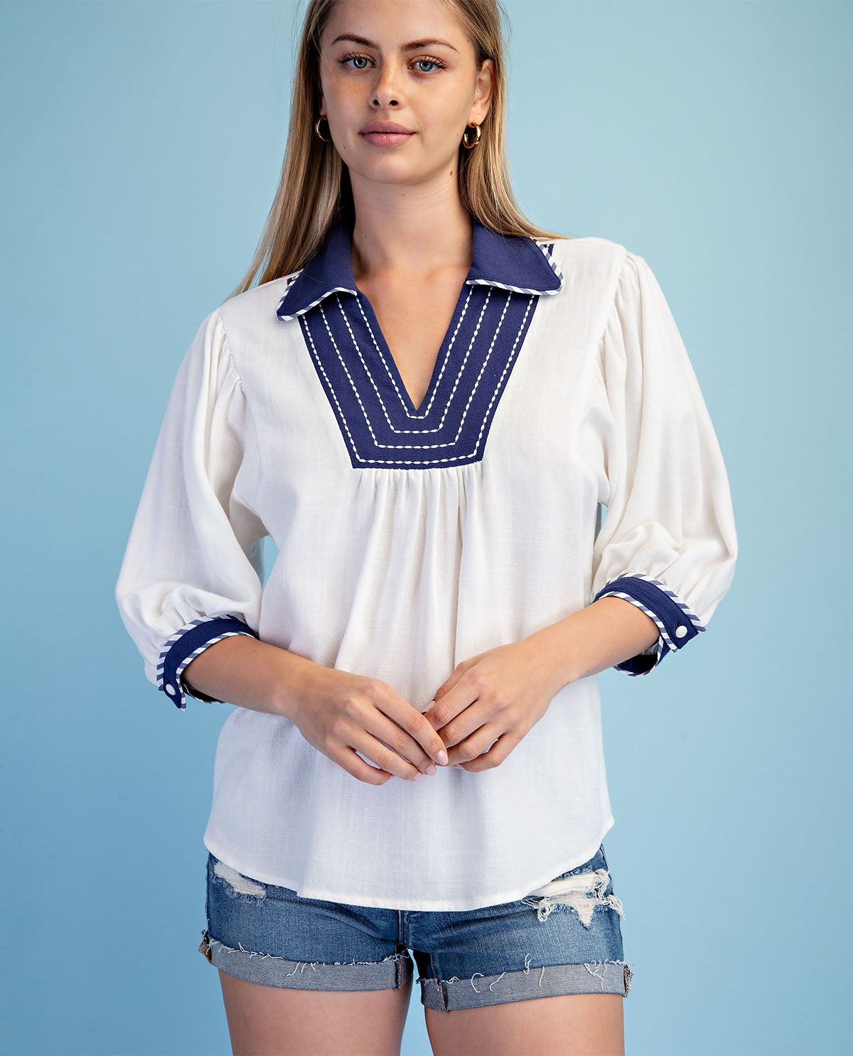 Woman wearing a white blouse with blue accents against a light blue background